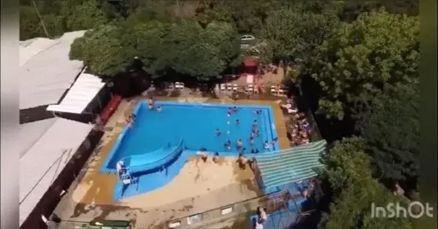 Vista aérea de piscina con tobogán entre árboles y construcciones