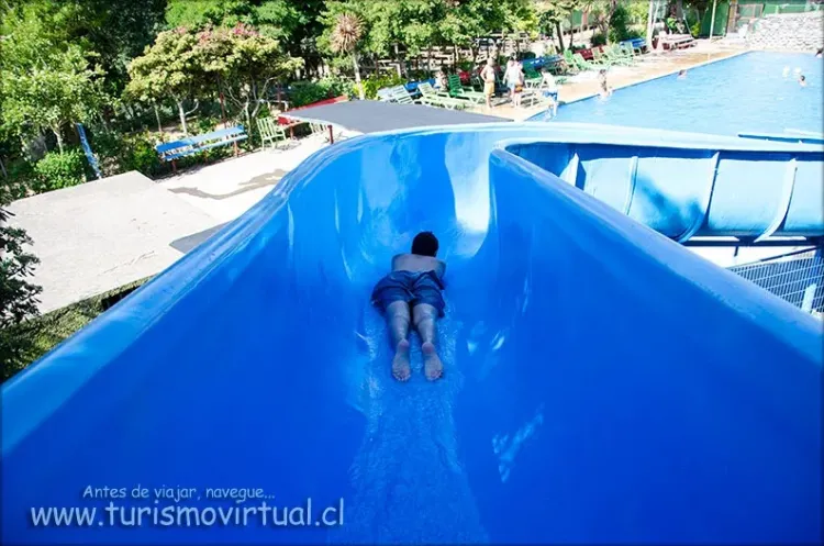 Persona descendiendo por un tobogán azul hacia la piscina